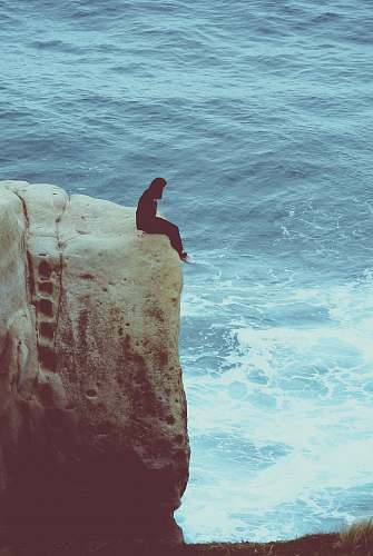 danger person sitting on edge of rock looking at sea water